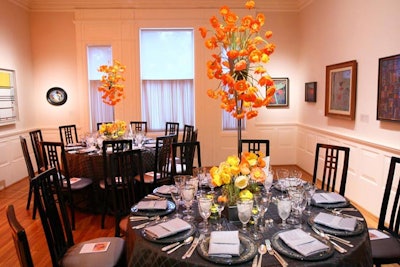 A smaller gallery used steel gray and black table settings accented with tall orange and yellow floral arrangements by Jack Lucky Floral Designs.