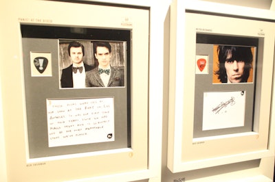 The auction items are signed guitar picks, which are presented alongside a photograph of the band or musician, as well as a note about where the plectrum was last used.