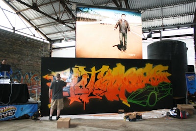 Graffiti artist Chad Tyson tagged the Hot Wheels logo underneath a jumbo screen showing the Indy 500 race and the Fearless at the 500 stunt.