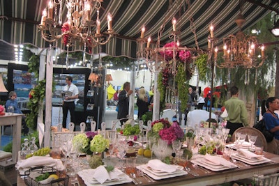 Town & Country Event Rentals showed off its new 'vineyard' collection, pieces with a rustic, cozy look evocative of an outdoor winery setting. In the exhibit, a striped canopy hung over a tabletop covered in lacy coverings. Fruits and artichokes served as accent pieces alongside etched glassware under hanging chandeliers.