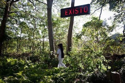 As part of Alejandro Moreno's installation, a male performer with a long ponytail ran on a treadmill while a neon sign flashed the words “exit,” “exist,” and “sexisto” above him. A treadmill whirred underneath his feet, but was intentionally obscured by underbrush.