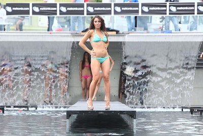 Models lined up underneath the waterfall at the far end of the pool before walking the runway.