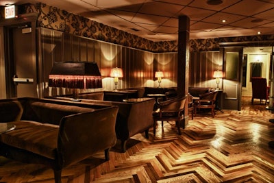 Fringed lamps, velvet sofas, and herringbone floors decorate the room.