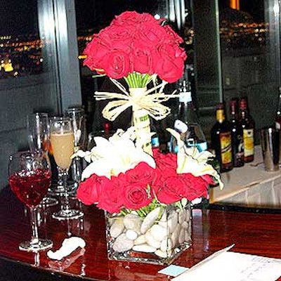 Lily and rose flower arrangements tied with raffia and set inside square vases filled with water and stones from New York Flowers & Plant Shed decorated the bar and dinner tables.