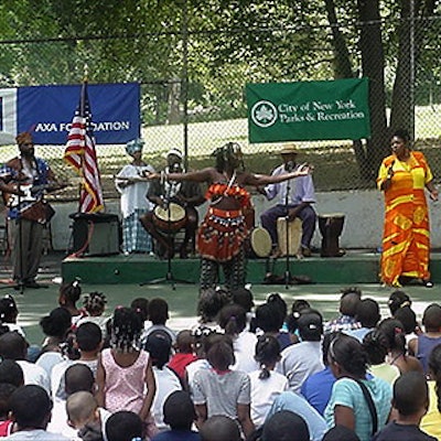 An audience of children watches the Kobla Dente Ensemble perform their African drum songs—part of the Arts in the Parks program. African storyteller Abike Jotayo stands at the rear of the stage on the left.