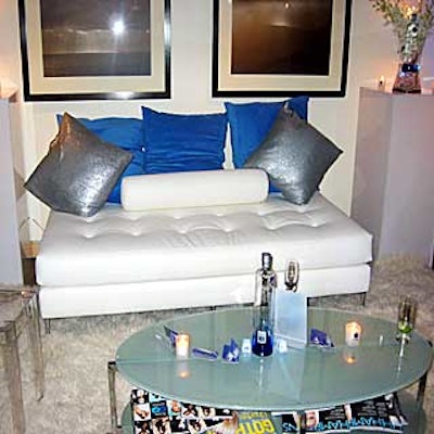 A white and blue lounge provided an intimate atmosphere using a white shag rug, white sofa with blue pillows, clear plastic chairs and white cubes.