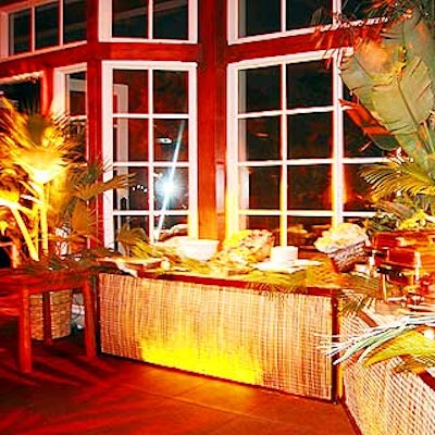 Planners decorated buffet tables with bamboo mats backlit with gold lights and lots of palm plants.