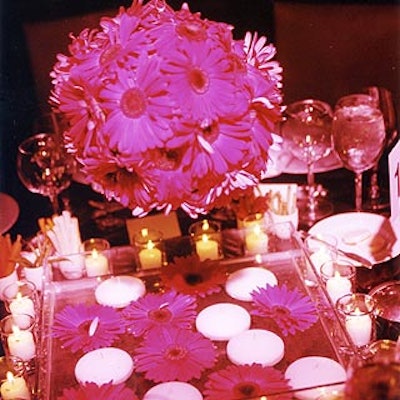 Hot pink gerbera daisy topiaries suspended from decorative Lucite chandeliers hovered over a square pool of water dotted with flowers and floating votives.