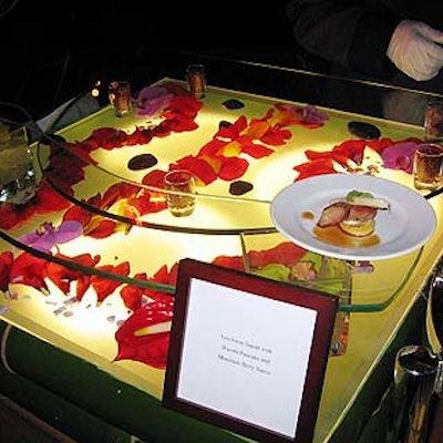 Asian-themed dishes were served at pretty serving stations made of square, white lightboards with red flower petals arranged on top. Orchids inside low square vases and votive cups filled with berries held up two curvy glass platforms above the lightboards where the individual servings were plated and served.