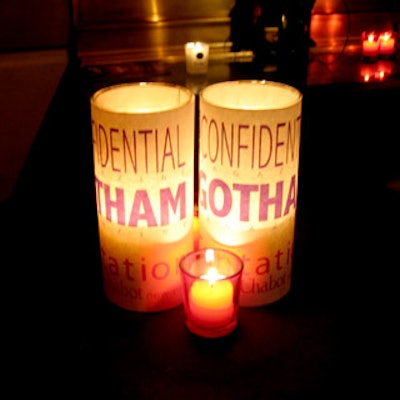 Pillar candles wrapped with Gotham and Tentation branding illuminated bars and tabletops around the main dance floor.