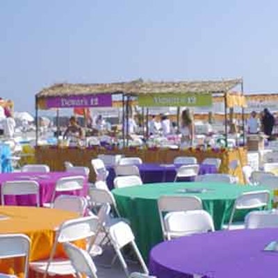 Tables dressed in colored linens surrounded tiki hut-like food stations for patrons to enjoy.