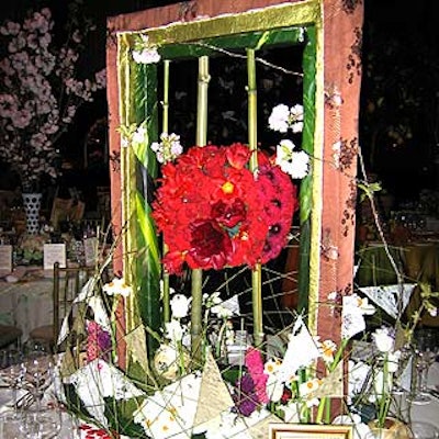 Japan-based floral designer Ayako Tachikawa's ikebana-inspired centerpiece featured a fabric-covered frame with a sphere of red and pink flowers suspended between two bamboo stalks. A grid of thin stalks and small bunches of daffodils and groupings of white flowers surrounded it.