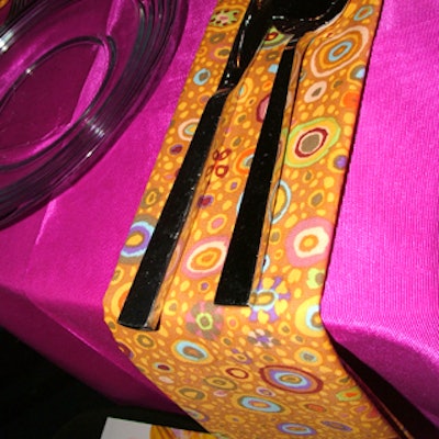 Adjacent to each guest's clear dinner plate, flatware sat atop colorful, patterned napkins that hung off the side of the table for a unique look.