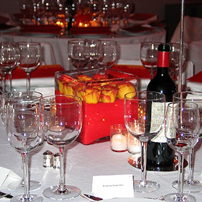White walls, tablecloths, chair covers, and dinnerware reflected the red light. Other details of the minimalist decor, designed by a team from Calvin Klein, included square glass vase centerpieces filled with red gel and rosebuds.