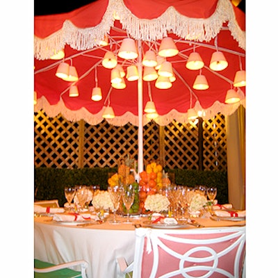 Kate Spade used a fringed beach umbrella hung with small lamps, glass vases of fruit, brightly colored chair cushions in beach-style chairs, and a bar cart stocked with gin and whiskey to give the table a 50's cocktail party vibe.