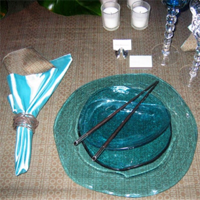 Chopsticks in a simple V shape topped a stack of three aquamarine-colored glass plates at Raymond Joseph of RJ Designs' table for faucet company Brizo. The brown tablecloth was printed with Brizo’s logo in a repeating pattern.