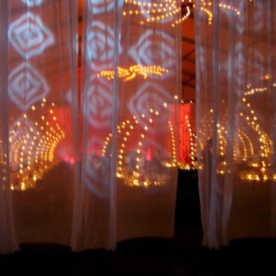 A sheer scrim adorned with decorative projections afforded a dramatic view of the dining area's arrangement of tall votive candelabra.