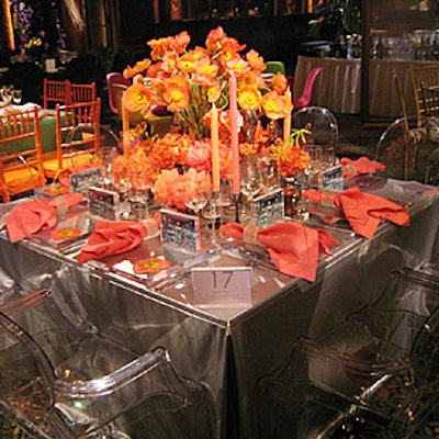Inspired by the Museum of Modern Art's mercury glass exhibit, Belle Fleur's table used a photograph of the collection by Christian Jaillite in plexiglass frames as place cards, and combined a silver-colored leather tablecloth with transparent chairs from Philippe Starck. The orange and coral centerpiece used striated taper candles and poppies, peonies, and gloriosa lilies in ceramic and mercury glass vases.