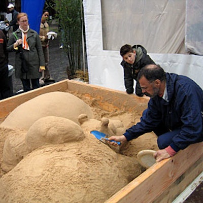 Sand sculptor G. Lynas crouched above a sandbox as children watched him sculpt a hippo.