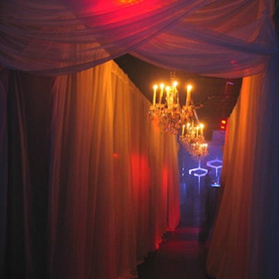 The hallway connecting the two main rooms was draped in sheer white fabric and accented with chandeliers and red lighting from Westbury National Show Systems.