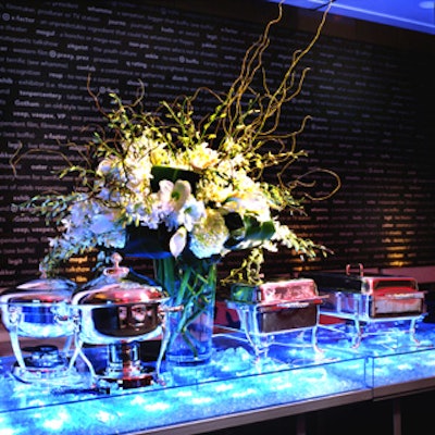 Guest grazed at two long buffet tables—cases of plexiglass and brushed metal enclosing crushed glass lit with fiber optics.