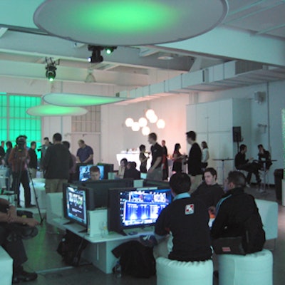 At Microsoft's Xbox 360 spring preview event, white leather lounge furniture surrounded square coffee tables, all topped with four flat-screen monitors attached to Xbox 360 consoles with different games.