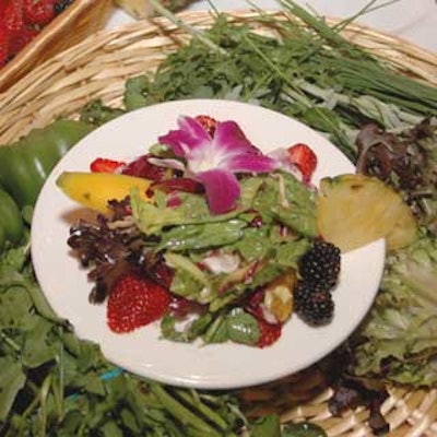A lot of salad served on a small plate was nestled into a charger topped with herbs and greens.