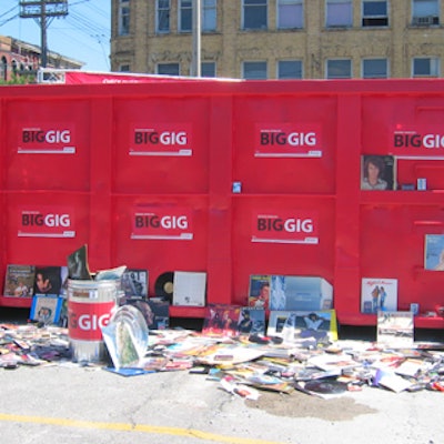 Record albums, audiocassettes and compact disks littered on the ground near the dumpster.