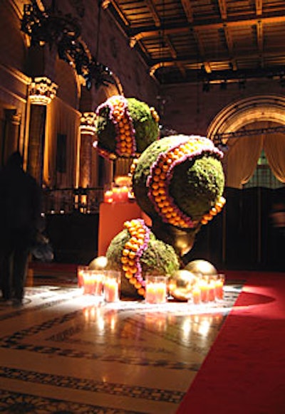 Dominating the entrance was event designer Ed Libby’s topiary, highlighting the evening’s wheel motif and orange and purple colors. The trilevel piece included three globes covered with blue curiosa roses and oranges as well as golden gazing balls and large orange pillar candles.