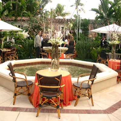 The event took place around a fountain, and featured scattered cocktail tables that had orange linens provided by Panache, dark-colored rattan chairs, and elaborate floral centerpieces.