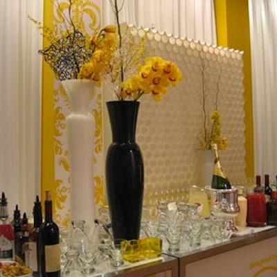 Tall black and white vases filled with unique decorative pieces and yellow blooms stood in front of a white honeycomb backdrop.