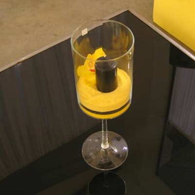 Wine glasses filled with yellow sand, blooms, and a black votive candle topped black coffee tables.