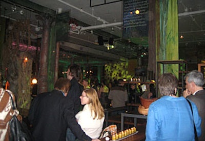 Overhead lighting cast a green tint on the space. Educational signs, screens showing promos for “The Green,” and branch and fabric installations hung from above.
