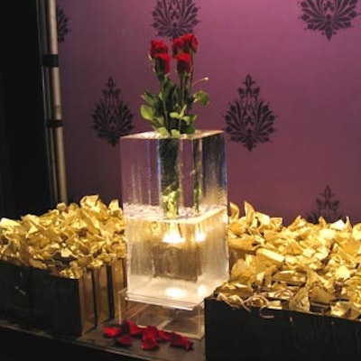 Small golden bags filled with parting gifts flanked a square ice vase holding red roses.