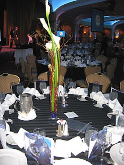 The 130 tables were covered with black tablecloths. Centerpieces were arranged in high and low vases, each filled with white calla lilies, roses, and grapevines floating in water, with a layer of blue stones at the bottom.