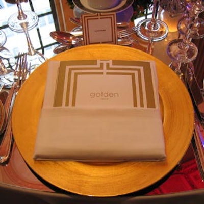Folded napkins atop gold charger plates held gold-framed event programs.