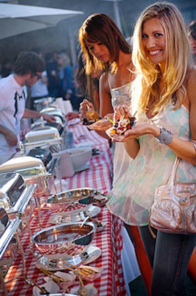 A BBQ buffet included shish kebabs, hot dogs, and ribs on tables topped with red checkered tablecloths.