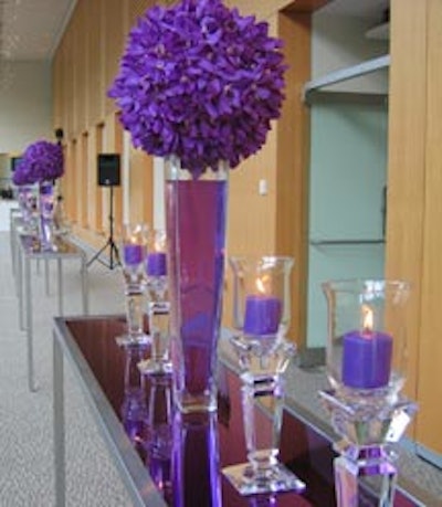 Purple candles in clear candleholders and purple orchid spheres atop vases filled with purple-hued water adorned tall long purple communal bar tables with mirrored tops.