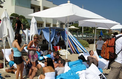 Guests lounged on white cushions and blue Boost towels on the sand under white sun umbrellas.