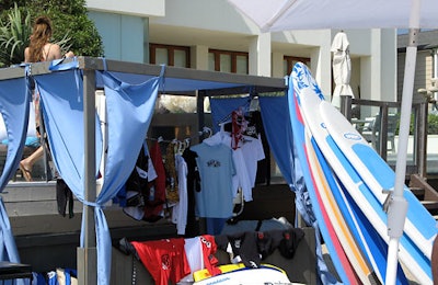 Boost-logoed Billabong gear and surfboards sat in and alongside a blue cabana on the sand.
