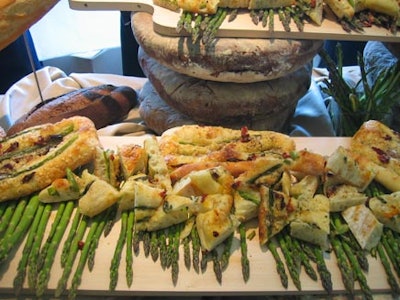 Fred’s Bread baked fresh snacks with raw asparagus displayed with a backdrop of massive bread loaves and other edible treats.