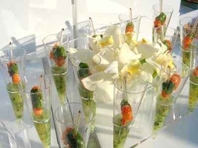 Summery soup shooters with shrimp on clear skewers were served in clear cone-shaped containers displayed in an acrylic stand.