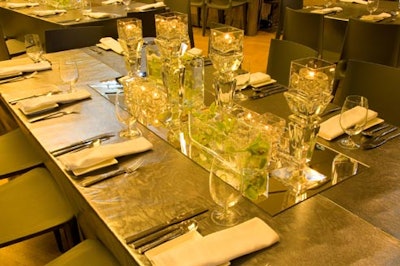 Crystal votive and pillar candle holders with yellow orchids on long mirrors topped custom “liquid metal” table linens from Chair-man Mills.