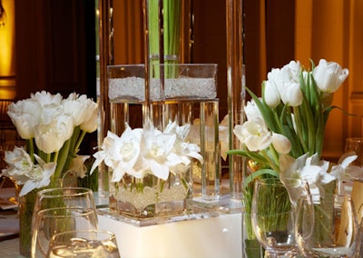 Always Flowers composed short, compact arrangements of white tulips and lilies in square glass vases to serve as centerpieces at a dinner event.