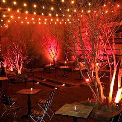 At night, the outdoor patio is lit with rows of lights strung across the walls, and ground lights illuminate the trees.