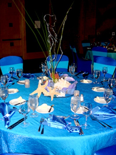 Tables were draped with dark and light blue linens, provided by Over the Top Rental Party Linens, topped with ocean-inspired centerpieces, and surrounded by blue spandex-covered chairs.