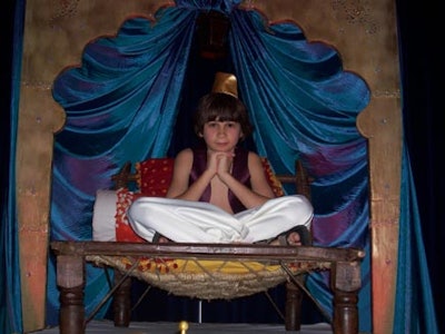 A performer perched on an antique Howda chair inside an Arabian tent.