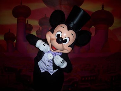 A costumed Mickey Mouse posed in front of a backdrop depicting an Arabian scene.