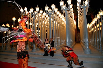 Costumed performers and stiltwalkers circulated around artist Chris Burden's light installation.