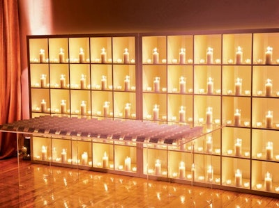 Lindsay Landman Events placed a display of candles in white shelves behind a clear table holding escort cards.